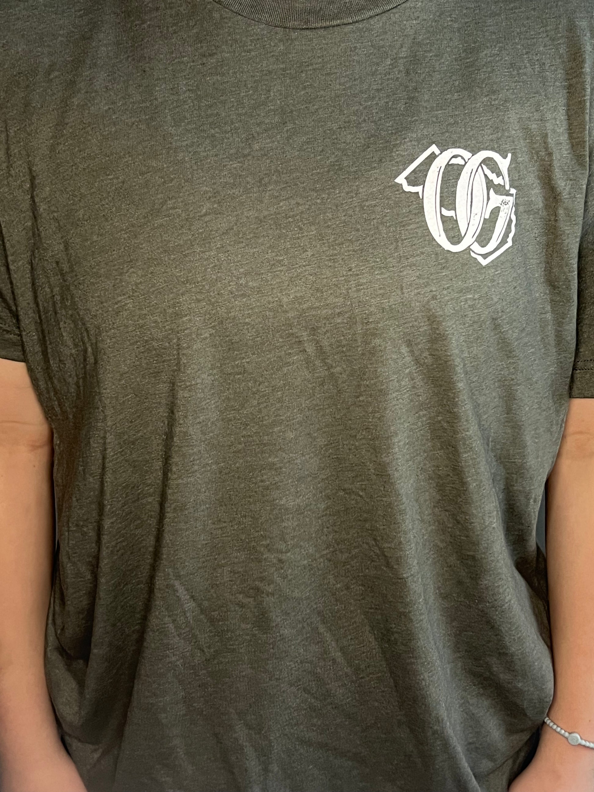 Close-up of a gray T-shirt featuring a white ‘OG’ logo on the left chest area, with the letters styled over an outline of the state of Georgia